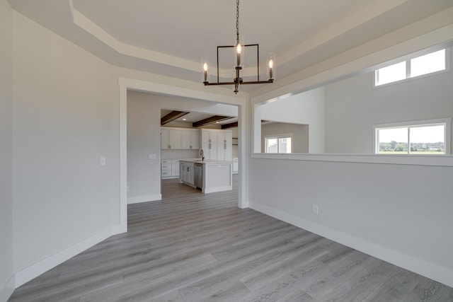 unfurnished living room featuring sink, light wood-type flooring, a raised ceiling, and a chandelier