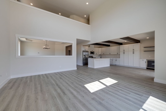 unfurnished living room with beam ceiling, light hardwood / wood-style floors, wine cooler, and a high ceiling