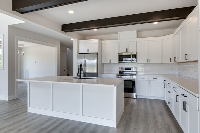 kitchen with stainless steel appliances, light hardwood / wood-style flooring, beamed ceiling, and white cabinetry