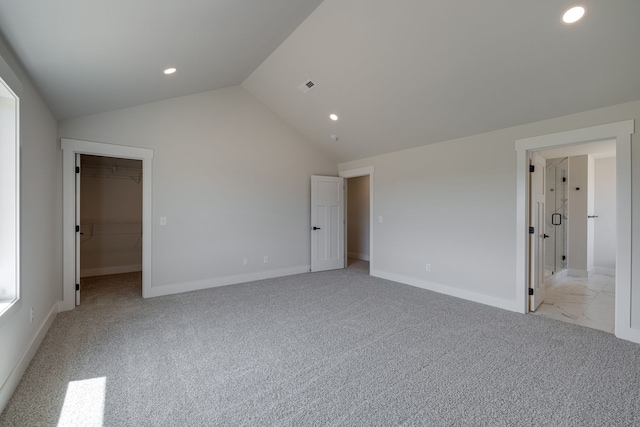 unfurnished bedroom with light carpet, vaulted ceiling, a spacious closet, and a closet