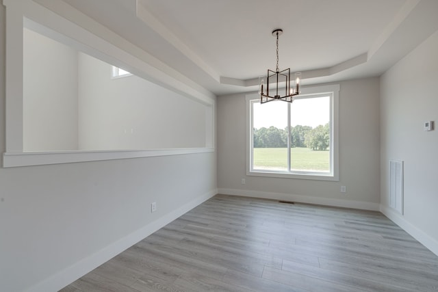 spare room featuring a notable chandelier, a raised ceiling, and light hardwood / wood-style floors