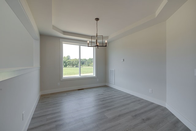 empty room with a notable chandelier, a tray ceiling, and hardwood / wood-style flooring