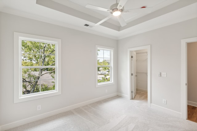 unfurnished bedroom with a walk in closet, a closet, ceiling fan, and light carpet