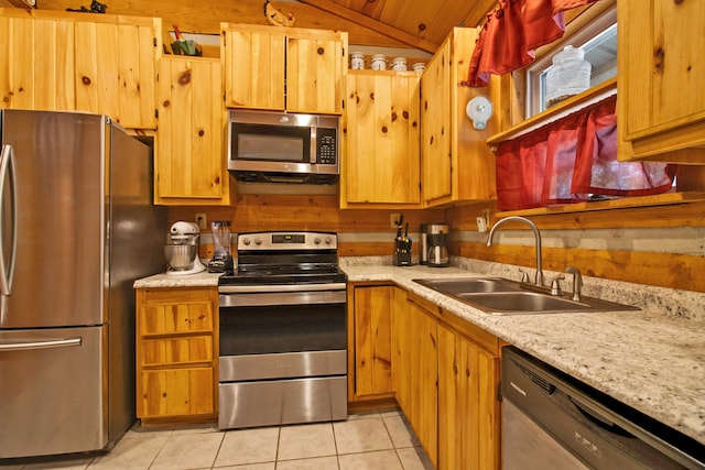 kitchen with stainless steel appliances, vaulted ceiling, wooden walls, sink, and light tile patterned floors