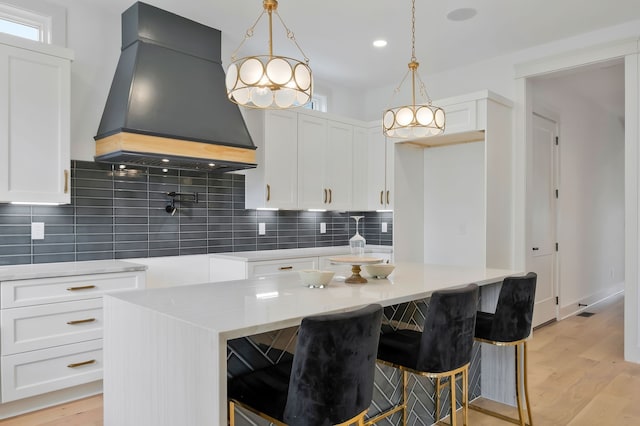 kitchen with custom range hood, a center island, light wood-type flooring, and tasteful backsplash