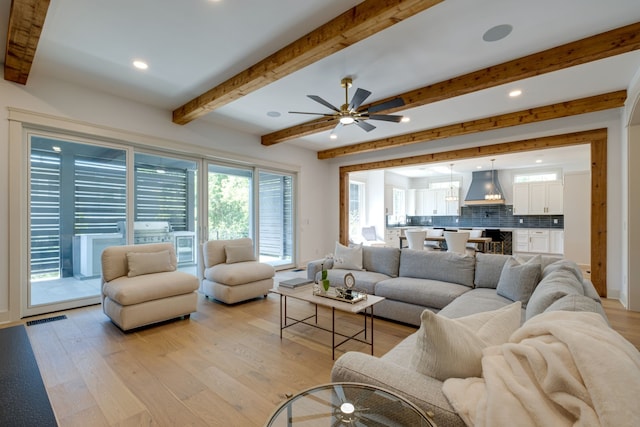 living room with light hardwood / wood-style floors, a wealth of natural light, ceiling fan, and beamed ceiling