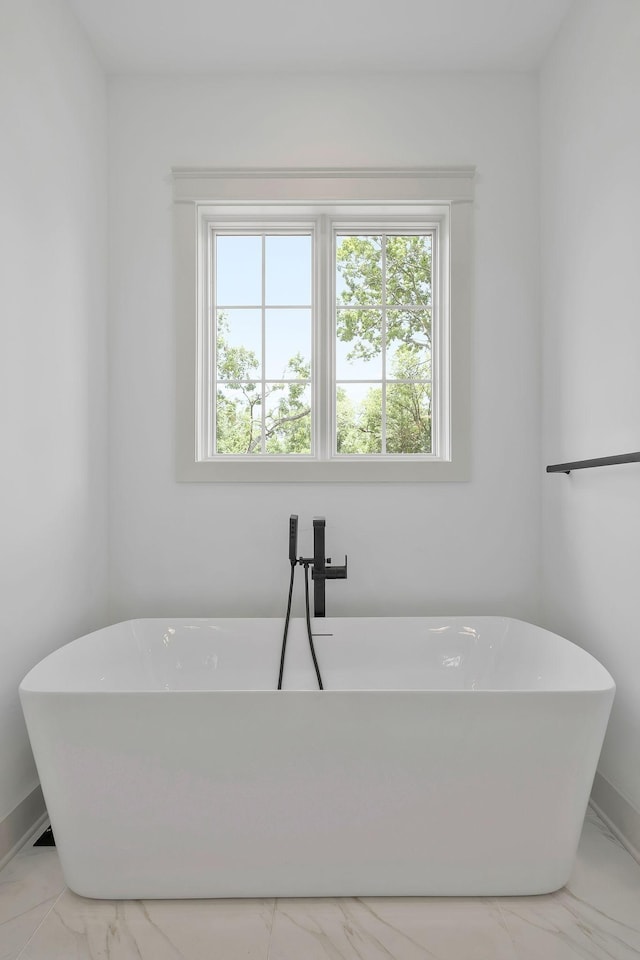 bathroom featuring marble finish floor, a freestanding tub, and baseboards