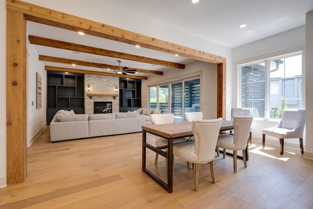 dining area with light hardwood / wood-style flooring, ceiling fan, a large fireplace, and beam ceiling