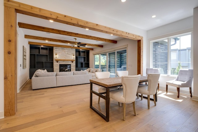 dining room featuring a stone fireplace, light wood finished floors, beamed ceiling, and a wealth of natural light