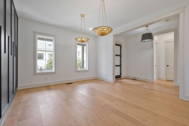 empty room with a notable chandelier and light wood-type flooring