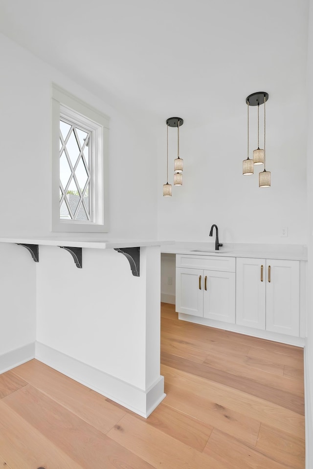 interior space featuring light wood-type flooring, sink, hanging light fixtures, and a kitchen breakfast bar