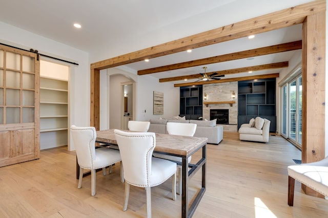 dining room featuring light hardwood / wood-style flooring, a large fireplace, built in features, beamed ceiling, and ceiling fan