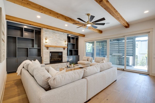 living room with a fireplace, beam ceiling, ceiling fan, and light wood-type flooring