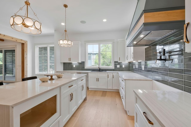 kitchen featuring a center island, hanging light fixtures, decorative backsplash, white cabinets, and light stone countertops