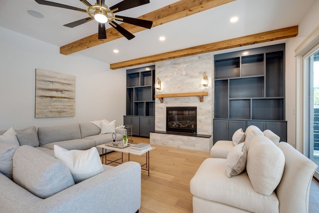 living room featuring ceiling fan, beam ceiling, light hardwood / wood-style flooring, and a stone fireplace