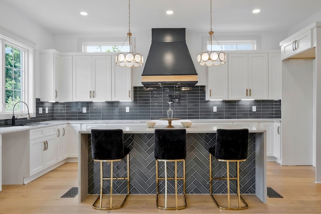 kitchen with premium range hood, white cabinetry, light wood-type flooring, and tasteful backsplash