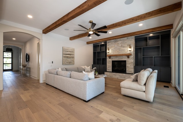 living room with ceiling fan, beam ceiling, light hardwood / wood-style flooring, and a fireplace