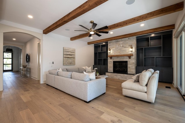 living room with arched walkways, recessed lighting, a fireplace, light wood-style floors, and beamed ceiling