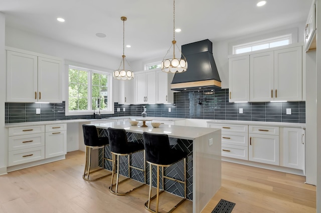 kitchen featuring decorative backsplash, white cabinetry, premium range hood, and light hardwood / wood-style floors