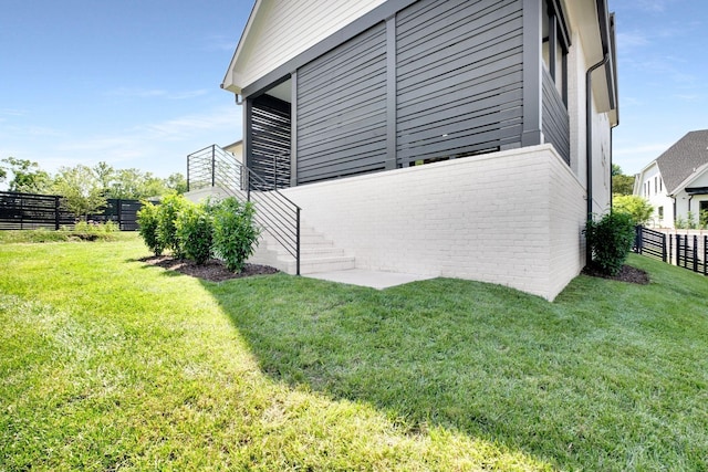 view of side of property with a yard, fence, stairway, and brick siding