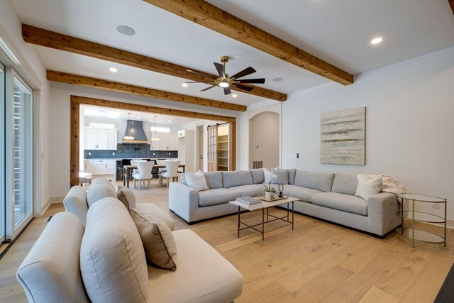 living room with ceiling fan, light hardwood / wood-style floors, and beamed ceiling