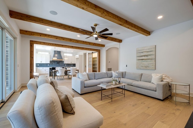 living area featuring light wood-style floors, arched walkways, beam ceiling, and recessed lighting