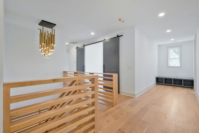 hallway with light hardwood / wood-style flooring, an inviting chandelier, and a barn door