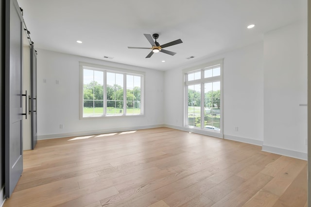 spare room featuring ceiling fan, light hardwood / wood-style flooring, and a barn door