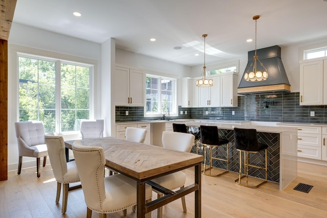 kitchen with light countertops, hanging light fixtures, white cabinetry, a kitchen island, and premium range hood