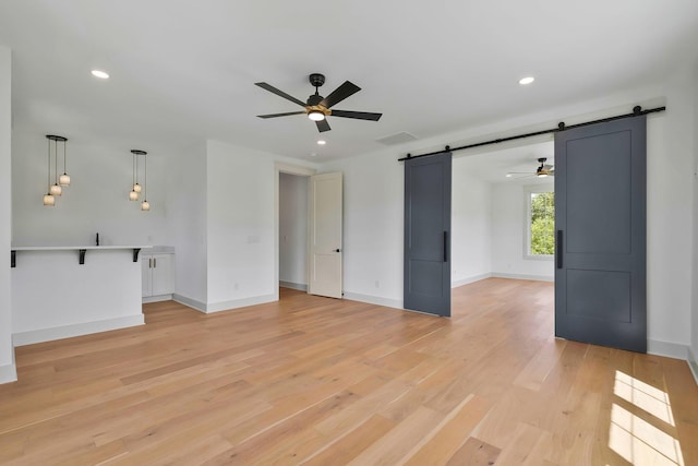 unfurnished living room featuring baseboards, a barn door, recessed lighting, and light wood-style floors