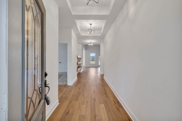 hall featuring a notable chandelier, a raised ceiling, and light hardwood / wood-style flooring