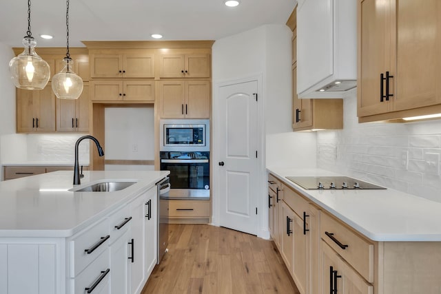 kitchen with sink, hanging light fixtures, stainless steel appliances, a kitchen island with sink, and light wood-type flooring