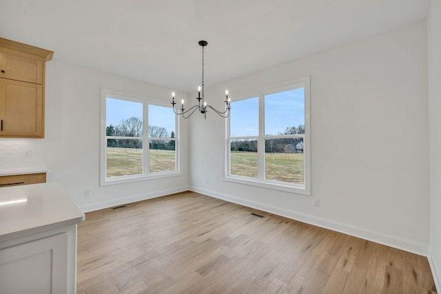 unfurnished dining area with light hardwood / wood-style flooring, a healthy amount of sunlight, and a notable chandelier