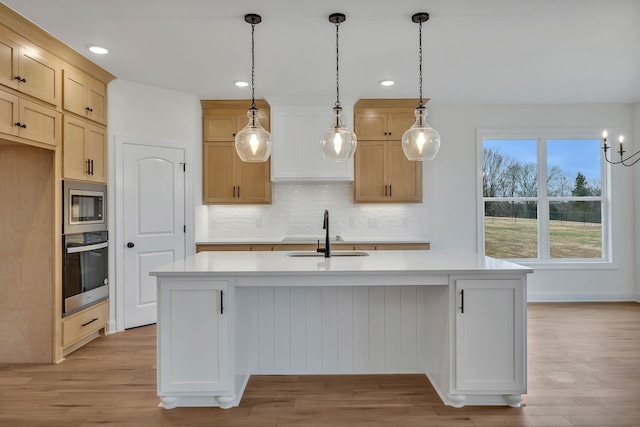 kitchen with sink, an island with sink, stainless steel appliances, and light hardwood / wood-style floors