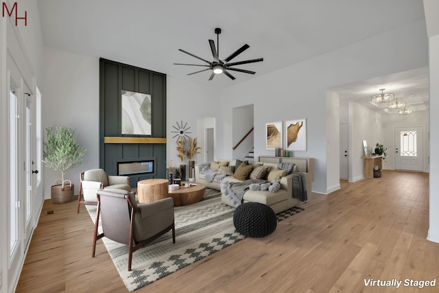 living room featuring ceiling fan with notable chandelier, a large fireplace, and light hardwood / wood-style floors