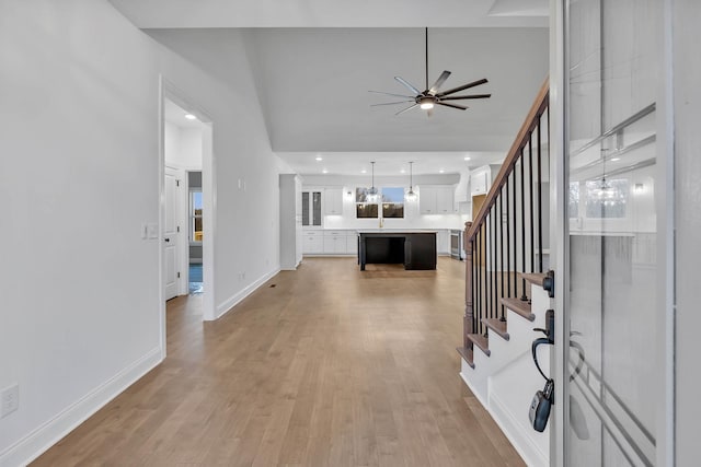 entryway with light wood-type flooring, a ceiling fan, baseboards, stairs, and vaulted ceiling