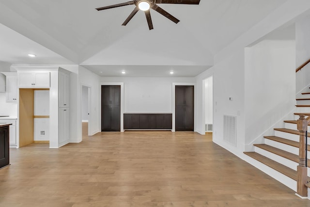 unfurnished living room with light wood finished floors, visible vents, ceiling fan, stairs, and vaulted ceiling