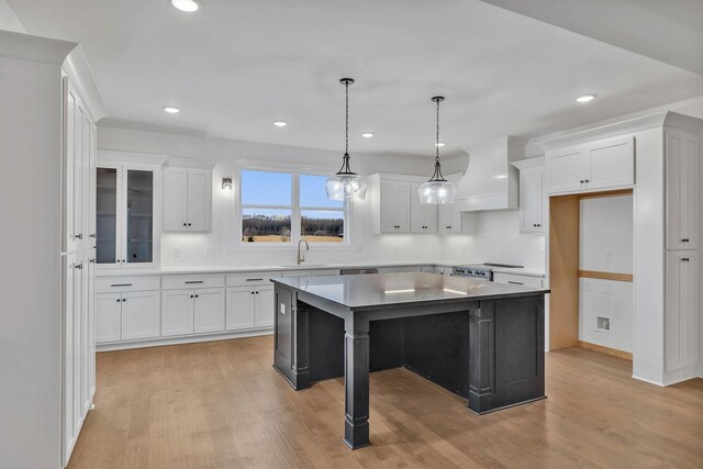 kitchen with light hardwood / wood-style floors, white cabinets, custom exhaust hood, and a kitchen island