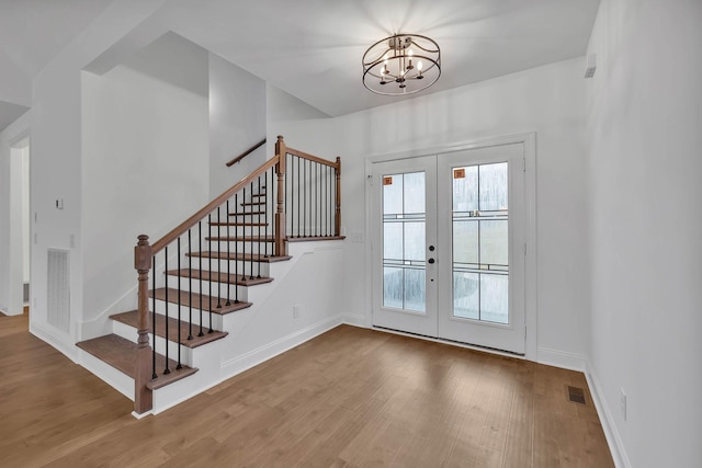 foyer featuring wood finished floors, stairway, a notable chandelier, and french doors