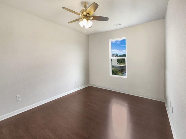 spare room featuring a ceiling fan, dark wood-type flooring, visible vents, and baseboards