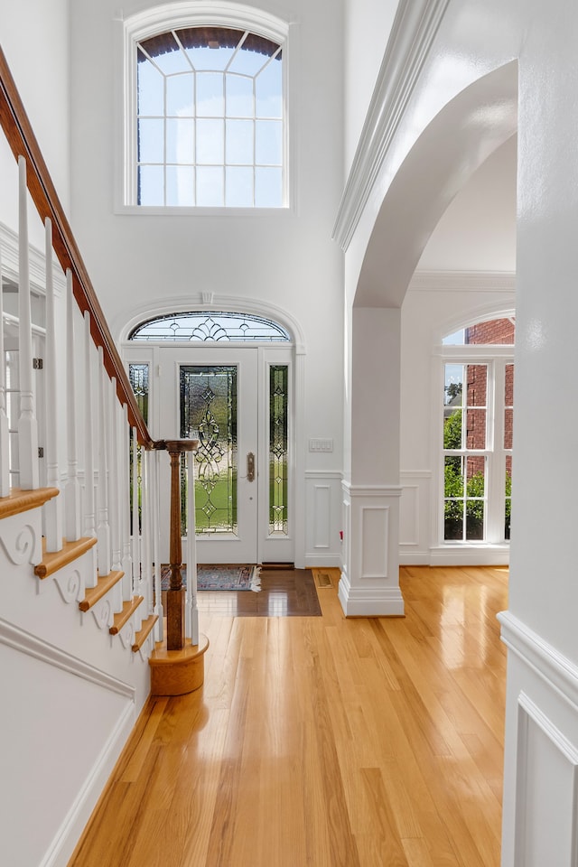 foyer entrance featuring light wood finished floors, arched walkways, wainscoting, a towering ceiling, and a decorative wall