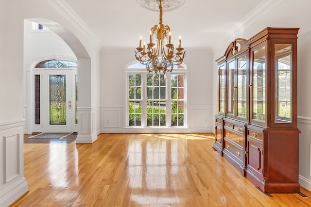 entryway with arched walkways, a notable chandelier, a decorative wall, ornamental molding, and light wood-type flooring