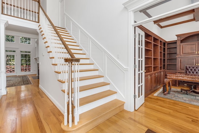 stairway with a high ceiling, wood-type flooring, and crown molding