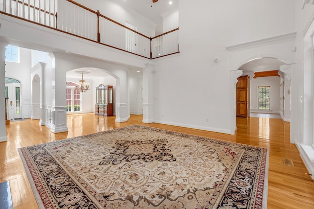 living room featuring a high ceiling, decorative columns, an inviting chandelier, and light hardwood / wood-style floors