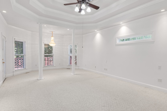 empty room with ornamental molding, carpet floors, a tray ceiling, and decorative columns