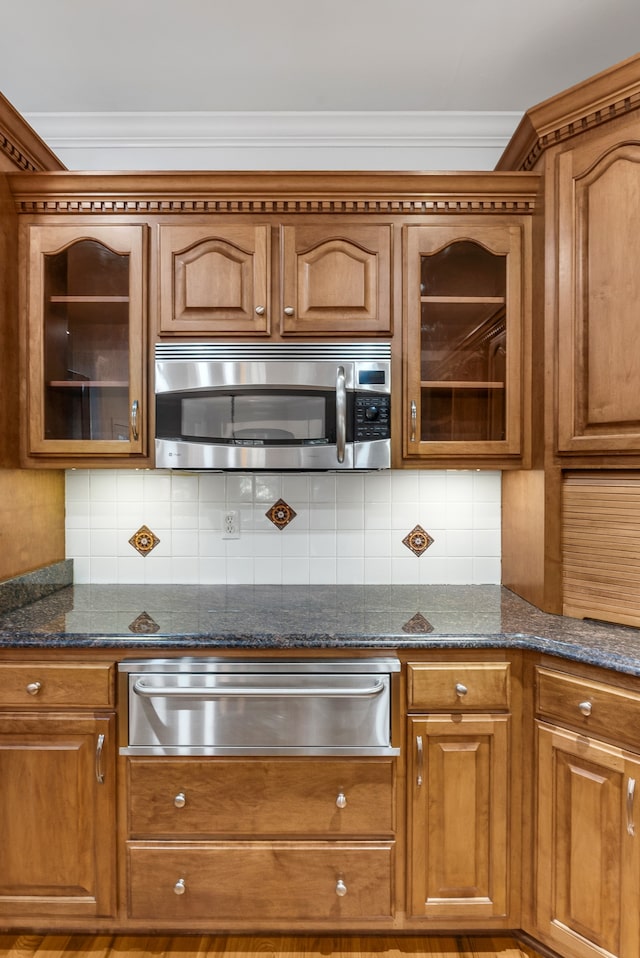 kitchen with backsplash, brown cabinets, a warming drawer, stainless steel microwave, and glass insert cabinets