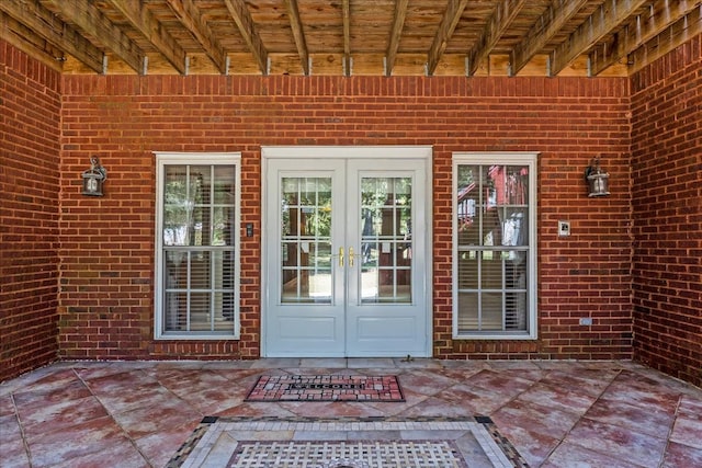 view of exterior entry with brick siding, a patio, and french doors