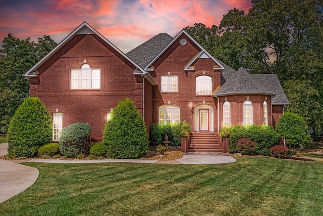 view of front facade featuring roof with shingles, a lawn, and brick siding