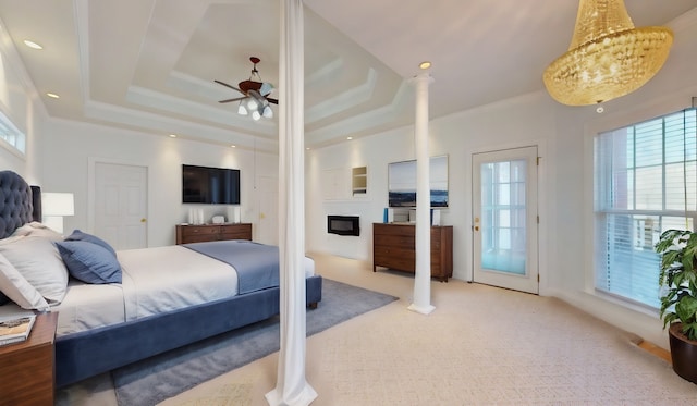 bedroom featuring light colored carpet, ornamental molding, a raised ceiling, and a glass covered fireplace