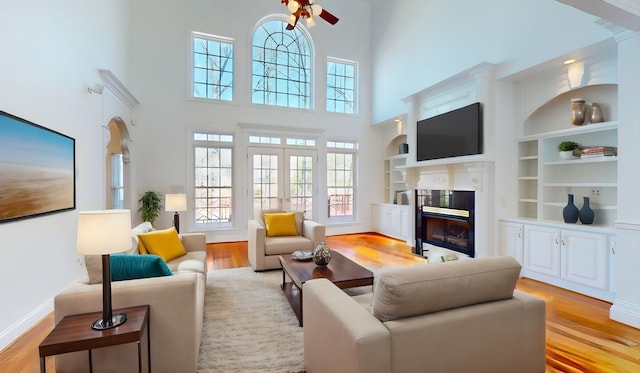 living room featuring built in shelves, ceiling fan, light hardwood / wood-style floors, and a high end fireplace